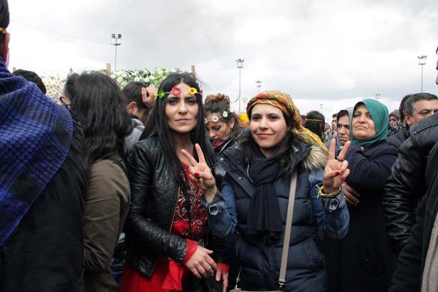 Zwei Frauen mit Blumenkränzen zeigen das Friedenszeichen in einer Menschenmenge.