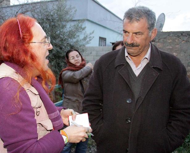 Eine Frau mit roten Haaren interviewt einen Mann mit Schnurrbart im Freien.