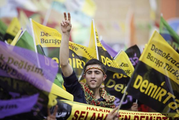 Ein junger Mann demonstriert mit Friedenszeichen und Fahnen der HDP im Hintergrund.