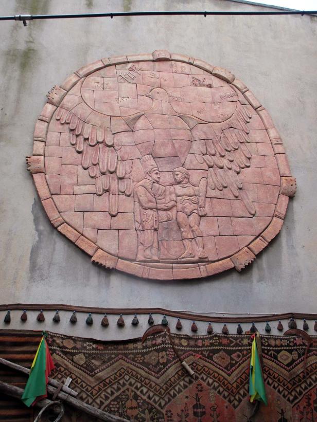 Ein Relief an einer Wand zeigt eine Taube, zwei Männer und das Wort „Frieden“ in verschiedenen Sprachen.