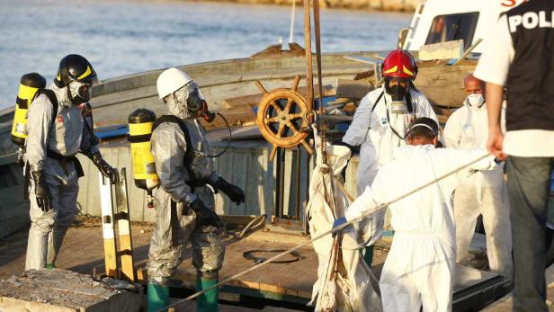 Mehrere Personen in Schutzanzügen und mit Atemmasken arbeiten auf einem Boot.