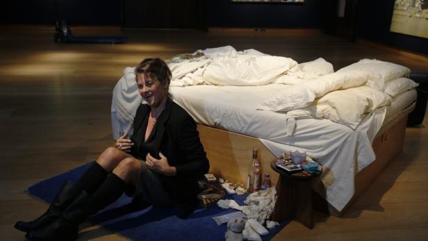 Eine Frau sitzt lachend vor Tracey Emins Installation „My Bed“.