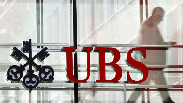 Das rote UBS-Logo ist an einem Gebäude angebracht, während eine Person im Hintergrund vorbeigeht.