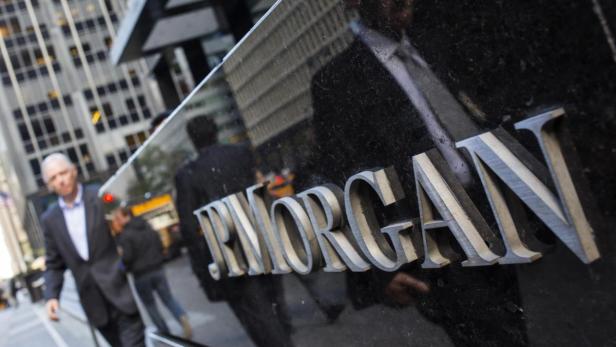 Das J.P. Morgan-Logo ist auf einer dunklen Oberfläche angebracht, während Menschen im Hintergrund vorbeigehen.