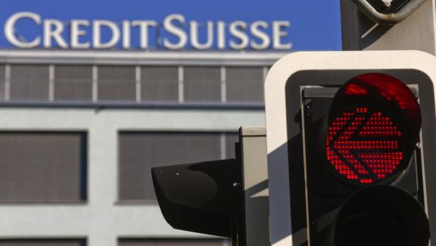 Eine rote Ampel mit einem Pfeil nach links vor einem Gebäude der Credit Suisse.