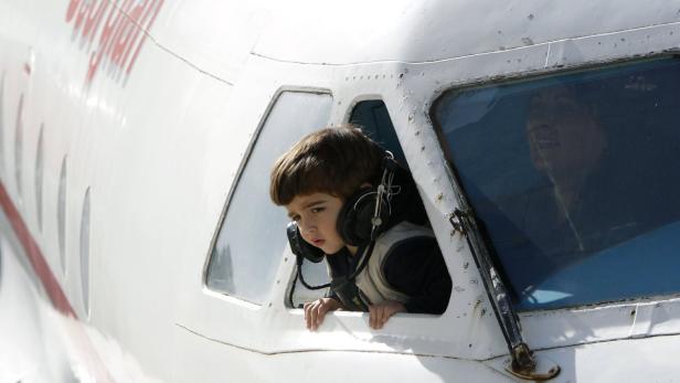 Ein Junge mit Kopfhörern schaut aus dem Fenster eines Flugzeugcockpits.