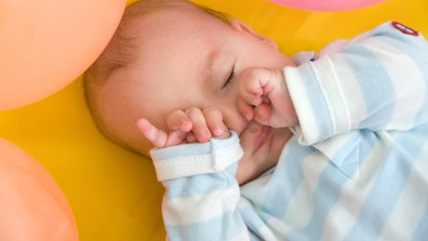 Ein schlafendes Baby liegt auf einer gelben Oberfläche mit bunten Ballons.