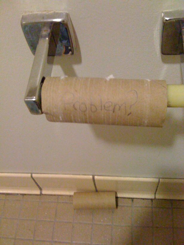 Eine leere Toilettenpapierrolle hängt am Halter, eine weitere liegt auf dem Boden. Auf der Rolle steht „Problem?".