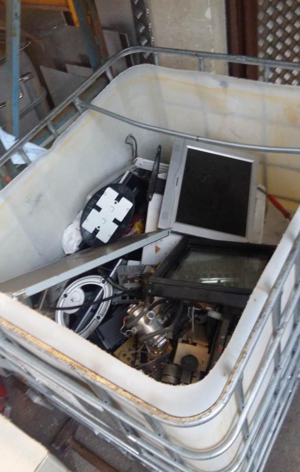 Ein Behälter gefüllt mit Elektroschrott, darunter ein Monitor und diverse elektronische Bauteile.