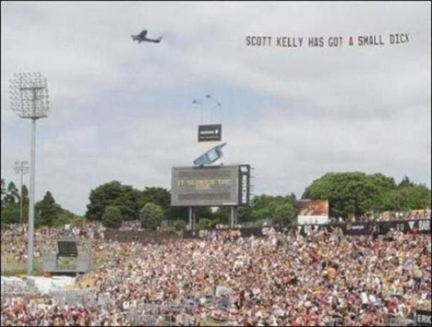 Über einem Stadion zieht ein Flugzeug ein Banner mit der Aufschrift „Scott Kelly has got a small dick“.