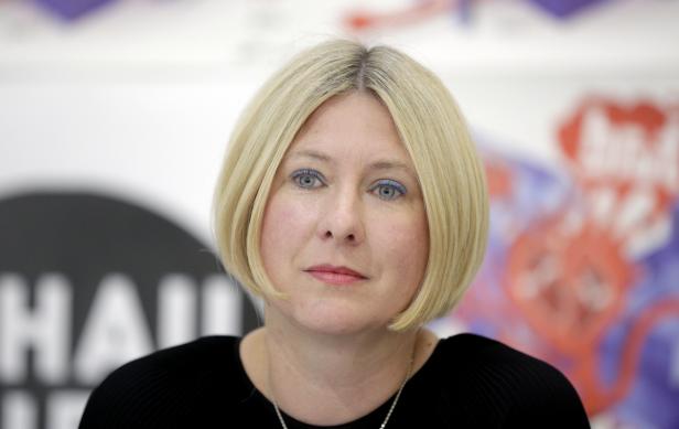Eine Frau mit blonden Haaren und blauem Eyeliner blickt in die Kamera.
