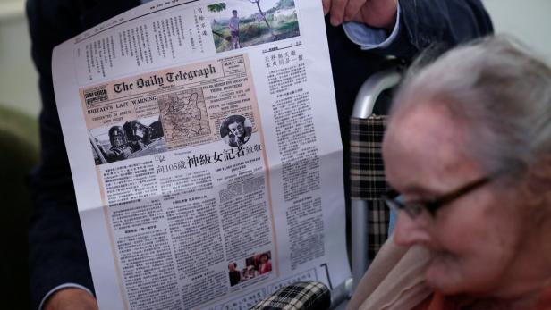 Eine ältere Frau liest eine Ausgabe des „Daily Telegraph“ mit Artikeln über den Zweiten Weltkrieg.