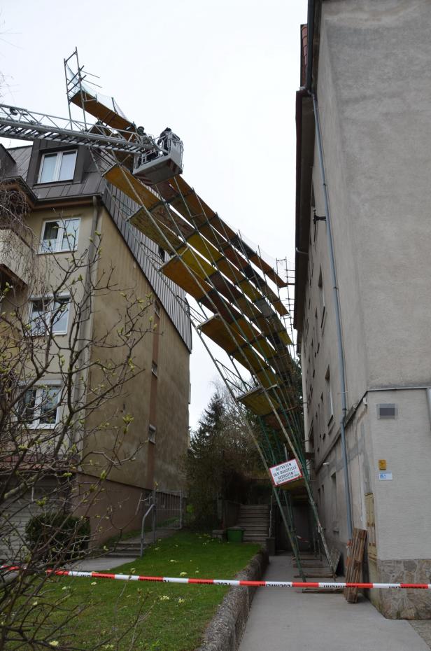 Ein Baugerüst verbindet zwei Gebäude, wobei ein Hubsteiger oben zu sehen ist.