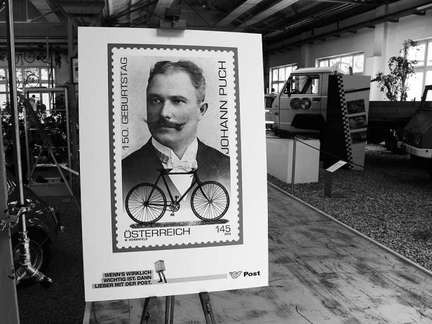 Eine Briefmarke zum 150. Geburtstag von Johann Puch mit seinem Porträt und einem Fahrrad.