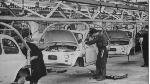 Arbeiter montieren Autos in einer Fabrikhalle am Fließband.