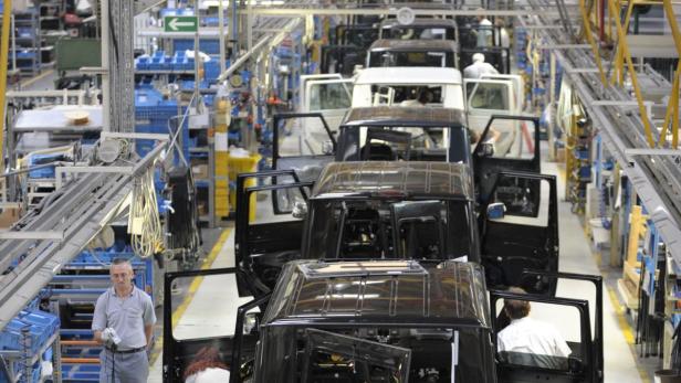 In einer Fabrik stehen mehrere schwarze Geländewagen mit geöffneten Türen.