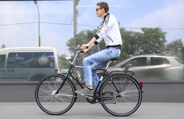 Ein Mann mit Sonnenbrille fährt ein schwarzes Fahrrad auf der Straße.