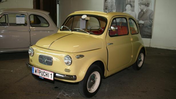 Ein gelber Fiat 500 „Puchi“ Oldtimer steht in einer Ausstellung.