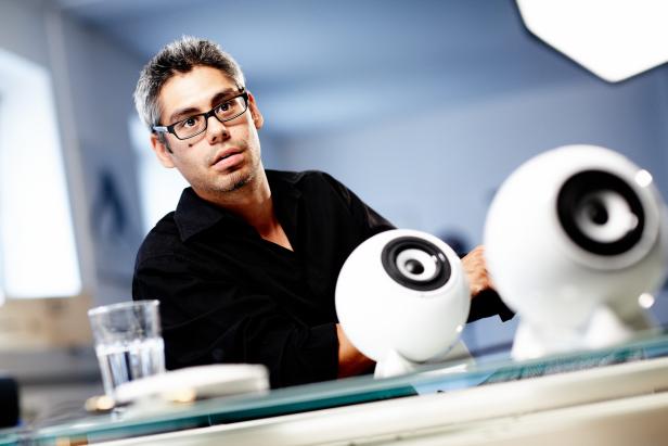 Ein Mann mit Brille betrachtet zwei kugelförmige Lautsprecher auf einem Tisch.