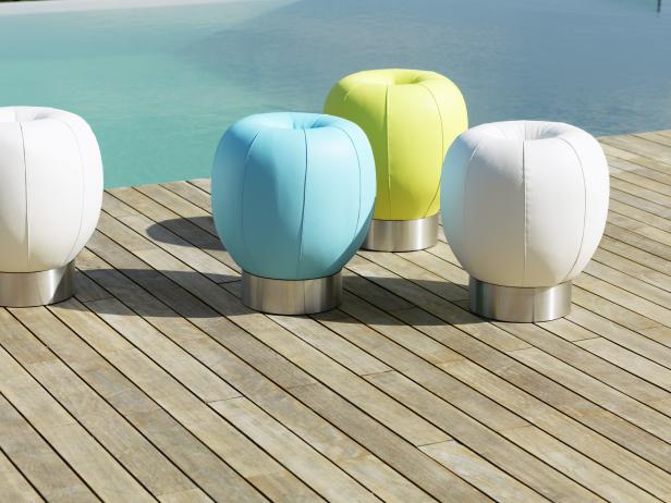 Mehrfarbige, runde Hocker stehen auf einer Holzterrasse neben einem Pool.