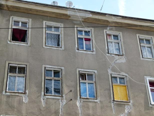 Die Fassade eines alten Hauses mit mehreren Fenstern und Rissen im Putz.