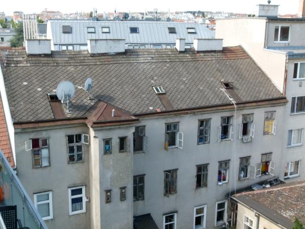 Ein Mehrfamilienhaus mit vielen geöffneten Fenstern und Satellitenschüsseln auf dem Dach.