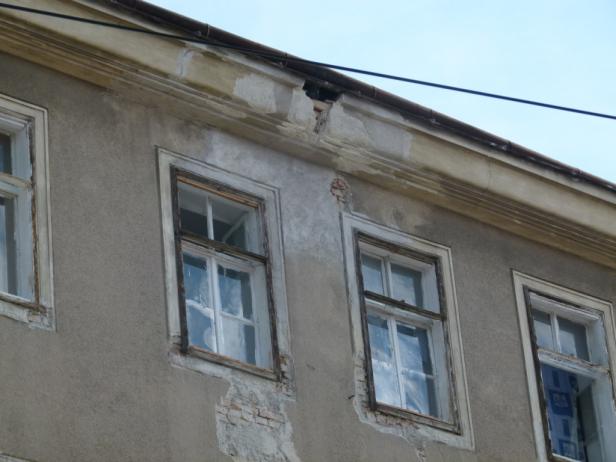 Die Fassade eines alten Gebäudes mit mehreren Fenstern und beschädigtem Putz.