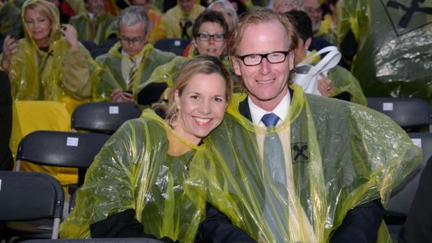 Ein lächelndes Paar in gelben Regenponchos sitzt auf einer Tribüne.