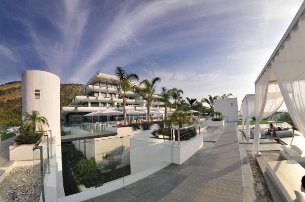 Ein modernes Hotelresort mit Palmen und Liegebereichen unter strahlend blauem Himmel.