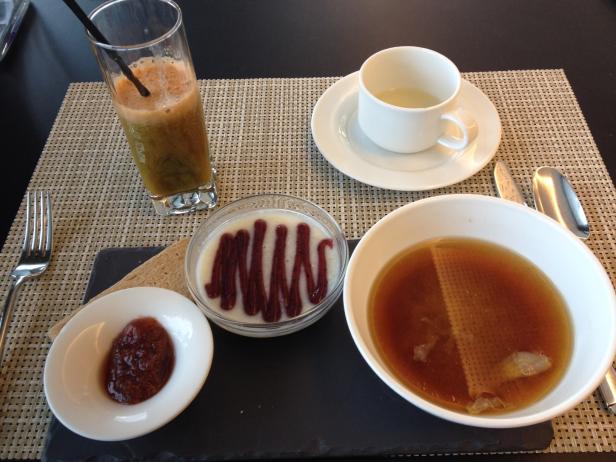 Ein gedeckter Tisch mit Suppe, Saft, Joghurt und Marmelade zum Frühstück.