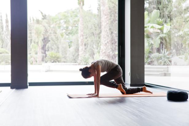 Eine Frau macht Yoga auf einer orangefarbenen Matte in einem hellen Raum.