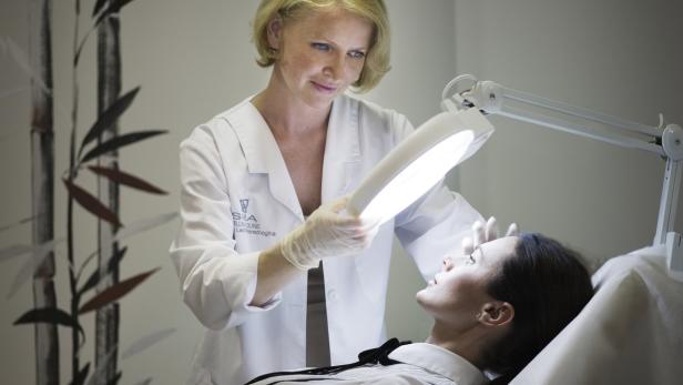 Eine Kosmetikerin untersucht das Gesicht einer Patientin unter einer Lampe.
