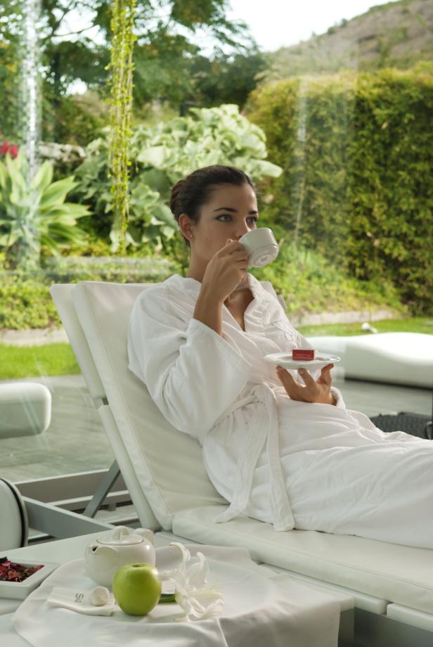 Eine Frau im Bademantel trinkt eine Tasse Tee auf einer Liege in einem Spa.