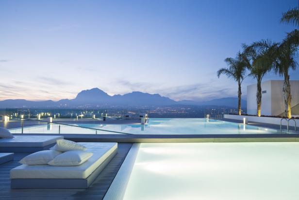 Ein Infinity-Pool mit Liegen und Blick auf eine Stadt und Berge in der Dämmerung.