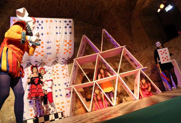 Eine Aufführung von „Alice im Wunderland“ mit Darstellern in Kostümen und einem Kartenhaus.