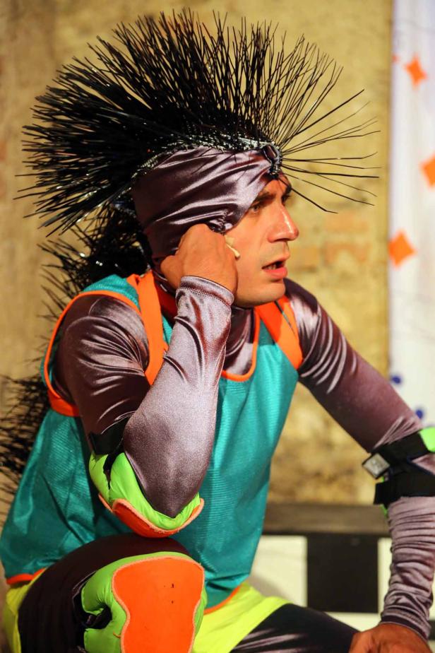 Ein Mann mit einem extravaganten Kostüm und einem stacheligen Kopfschmuck sitzt da.