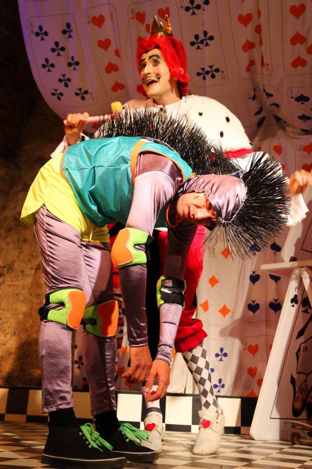 Zwei Darsteller in Kostümen auf einer Bühne mit Spielkartendekorationen.