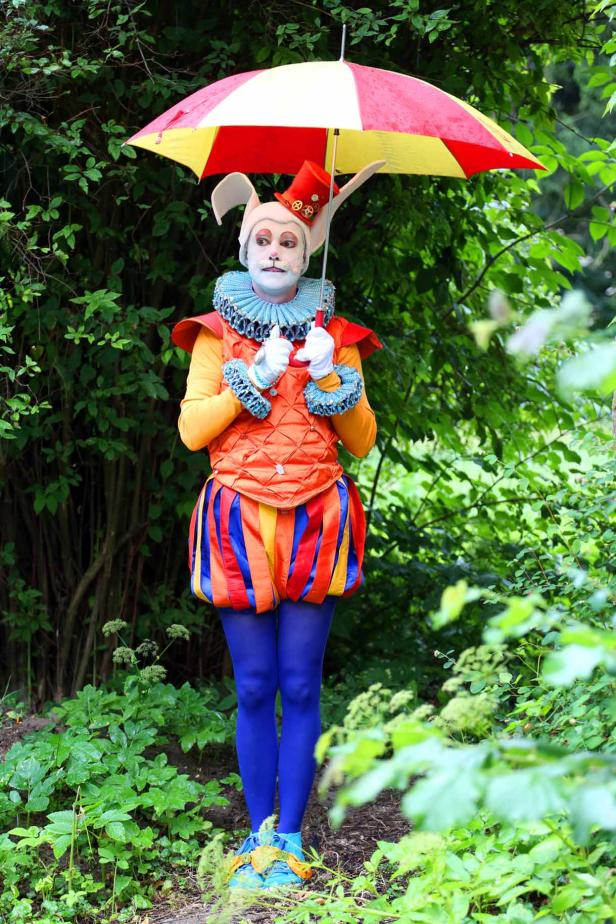 Ein Mann in einem bunten Hasenkostüm steht mit einem Regenschirm im Grünen.