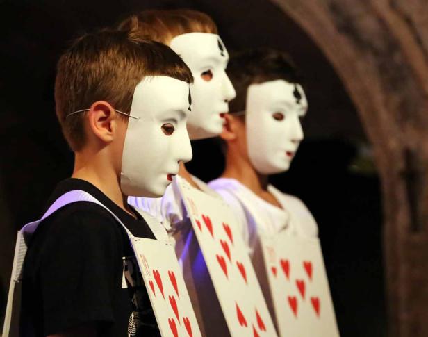 Drei Kinder tragen weiße Masken und Spielkartenkostüme.