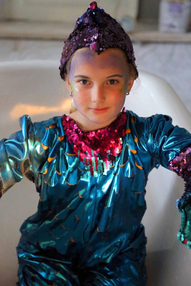 Ein Mädchen in einem schuppigen Kostüm mit Pailletten und passendem Hut.