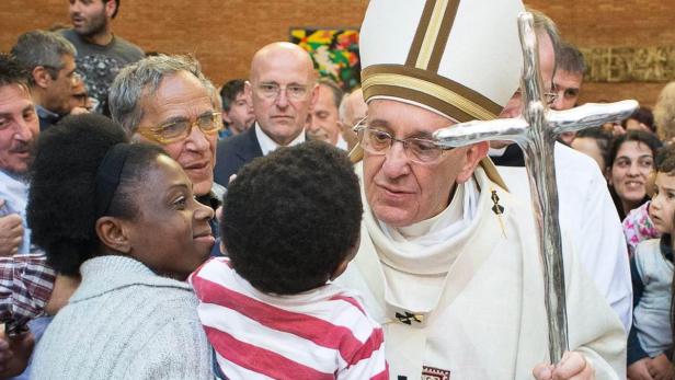 Papst Franziskus segnet ein Kind mit einem silbernen Kreuz.