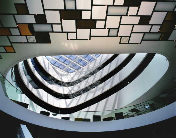 Blick in das Innere eines modernen Gebäudes mit mehreren Etagen und einem Glasdach.