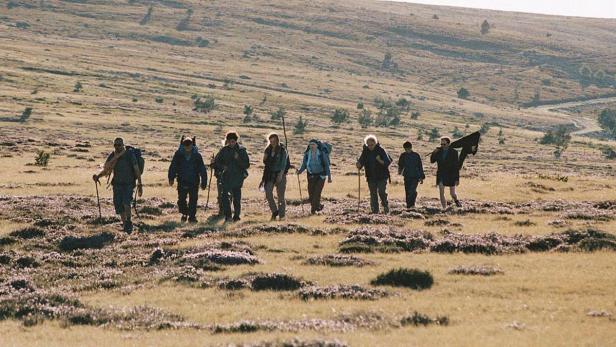 Eine Gruppe Wanderer durchquert eine hügelige Landschaft.