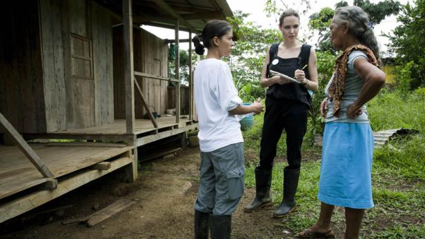 Angelina Jolie spricht mit zwei Frauen vor einem einfachen Holzhaus.
