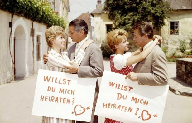 Zwei Paare halten Schilder mit der Aufschrift „Willst du mich heiraten?“.