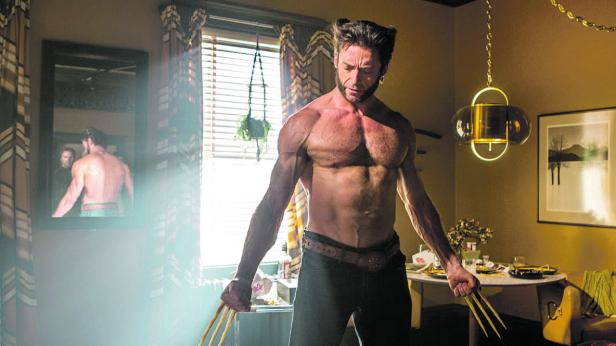 Hugh Jackman als Wolverine steht mit ausgefahrenen Krallen in einem Zimmer.