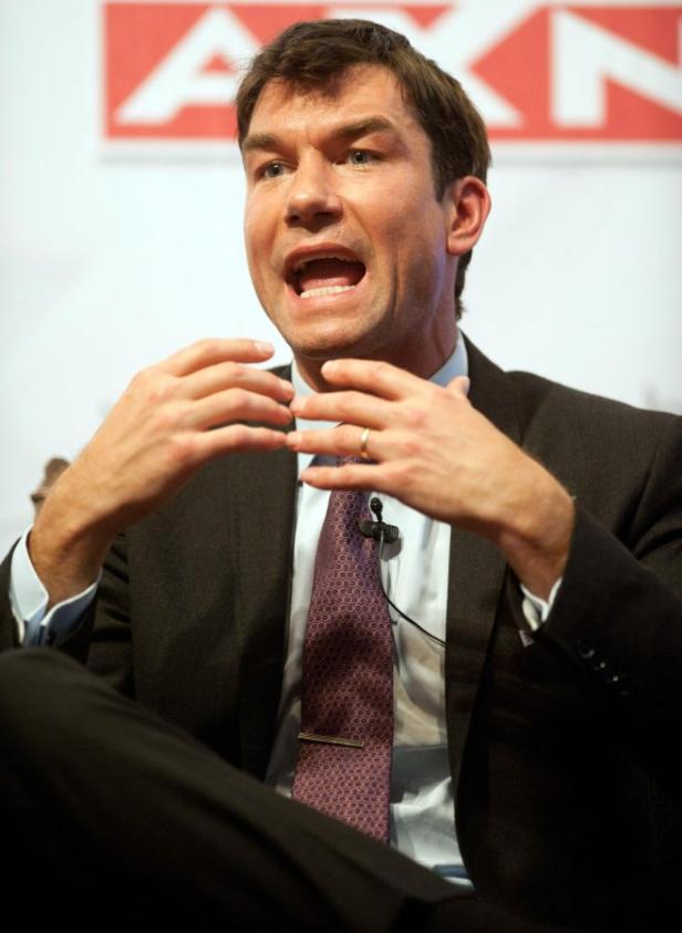 Ein Mann in Anzug gestikuliert während einer Präsentation vor einem AXN-Logo.