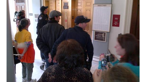 Eine Gruppe von Menschen steht in einem Flur, einige mit Handschellen gefesselt.