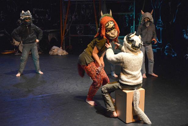 Eine Theaterszene mit vier Darstellern in Tiermasken und Kostümen auf einer dunklen Bühne.
