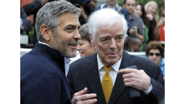 George Clooney im Gespräch mit einem Mann im Anzug vor einer Menschenmenge.